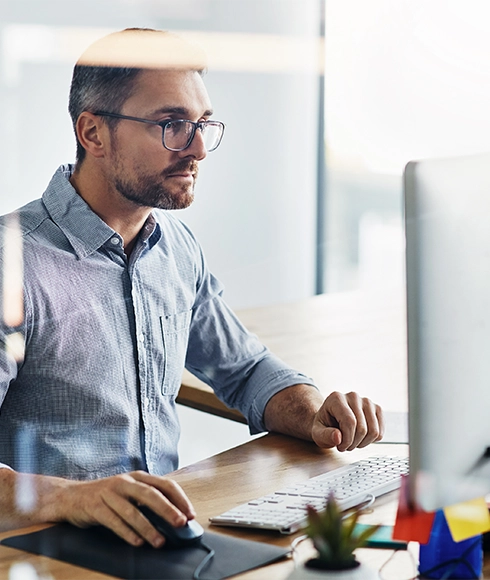 Un homme portant une chemise bleu clair travaille sur un ordinateur pour illustrer les raisons de transformer son pilotage financier avec Prophix One.
